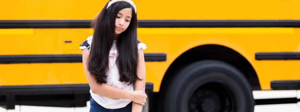 Girl sadly standing beside a school bus
