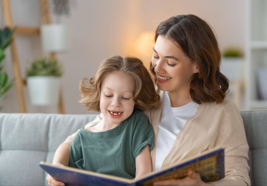 Parent and child smiling while reading together on a couch at home